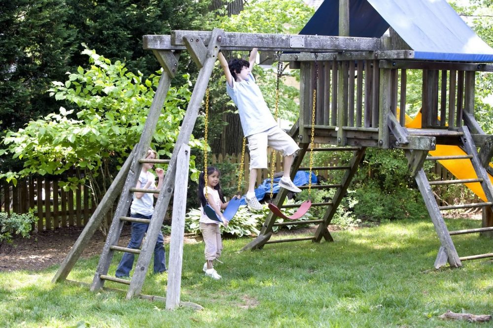 A picture containing grass, outdoor, tree, climbing frame showing three children playing together